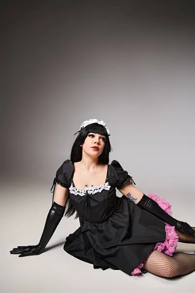 Atractivo cosplayer sexy en traje de criada negro posando activamente y mirando hacia otro lado en el fondo gris - foto de stock