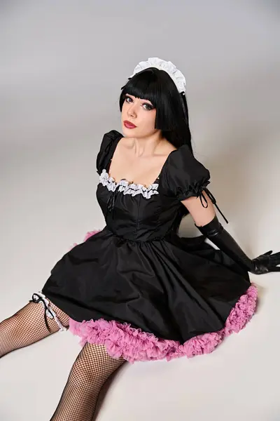 Glamorous sexy female cosplayer in tempting maid costume looking at camera on gray background — Stock Photo
