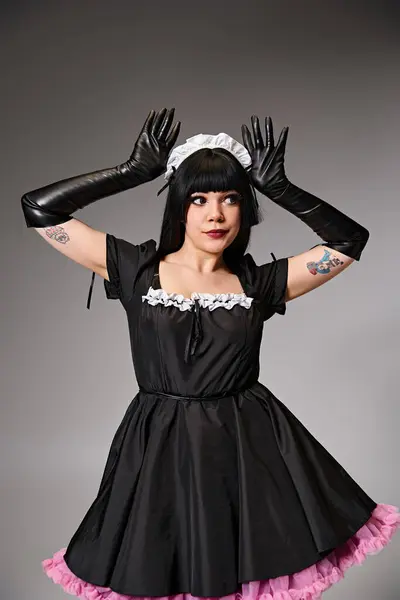 Tentadora cosplayer femenina en traje de criada mostrando orejas de neko y mirando hacia otro lado en el fondo gris - foto de stock