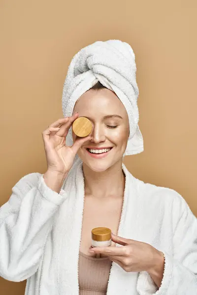 A beautiful woman exuding natural beauty, with a towel on her head, holding cream. — Stock Photo
