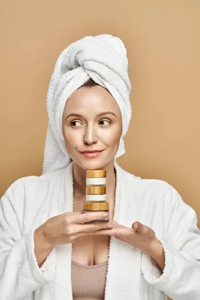 Une femme sereine avec une serviette sur la tête tenant un pot de crème, mettant en valeur la beauté naturelle et la routine d'autosoin. — Photo de stock