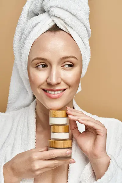 Una mujer con una toalla en la cabeza sostiene elegantemente la crema, encarnando la relajación y la elegancia. - foto de stock