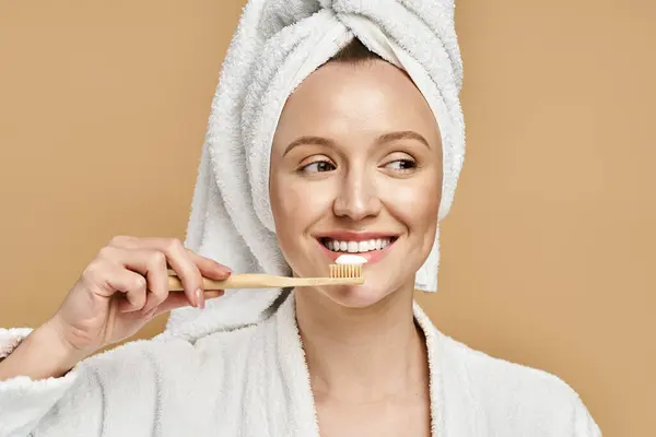 Uma mulher bonita com uma toalha enrolada em torno de sua cabeça escovando os dentes em uma pose animada e natural. — Fotografia de Stock