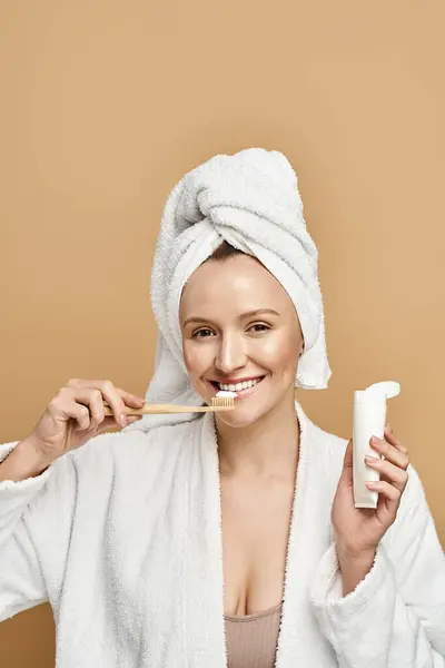 A woman with natural beauty brushing her teeth while wearing a towel on her head. — Stock Photo
