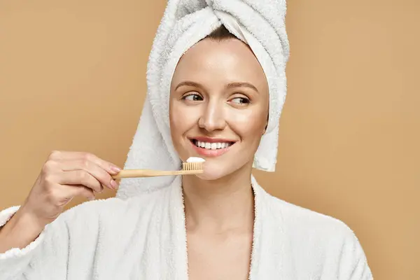 An attractive woman with a towel on her head is brushing her teeth in a daily morning routine. — Stock Photo