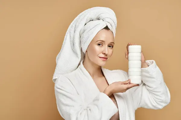 Uma mulher em um manto mostra sua beleza natural enquanto segura um tubo de creme. — Fotografia de Stock