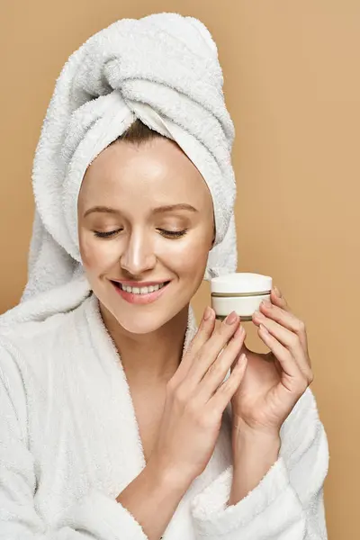 Una mujer seductora mostrando belleza natural, sosteniendo un frasco de crema en una bata de baño. - foto de stock