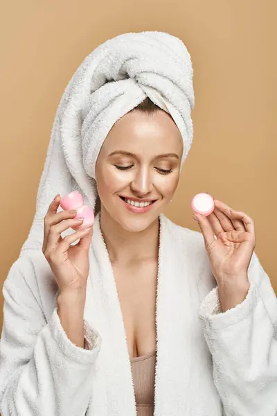 Una mujer de belleza natural envuelta en una toalla sostiene dos cremas en un entorno de spa sereno. - foto de stock