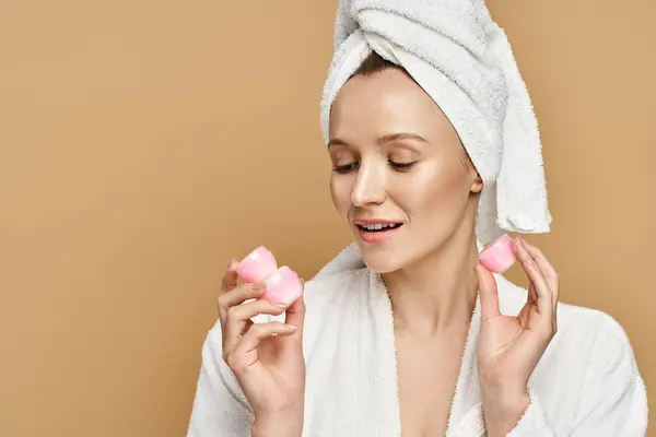 Uma beleza natural com uma toalha na cabeça segura dois cremes em uma pose caprichosa. — Fotografia de Stock