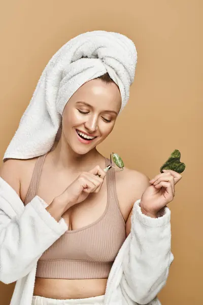Женщина с полотенцем на голове держит лицо ролика, демонстрируя естественную красоту и связь со здоровым питанием. — стоковое фото