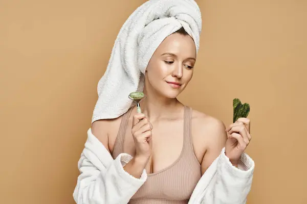 A natural beauty woman with a towel on her head holding face roller. — Stock Photo