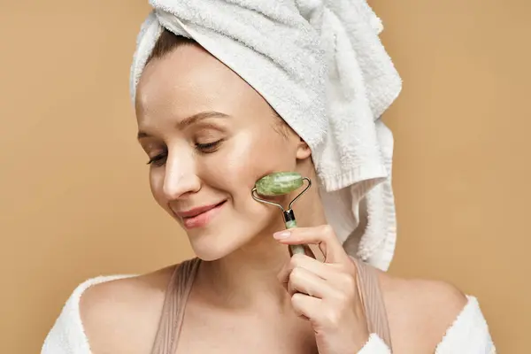 Una donna graziosa con un asciugamano sulla testa è visto tenendo rullo viso in un modo in bilico. — Foto stock