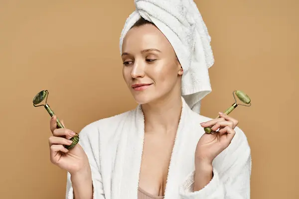 Una mujer con una toalla en la cabeza sosteniendo delicadamente el rodillo facial, exudando belleza natural y elegancia. - foto de stock