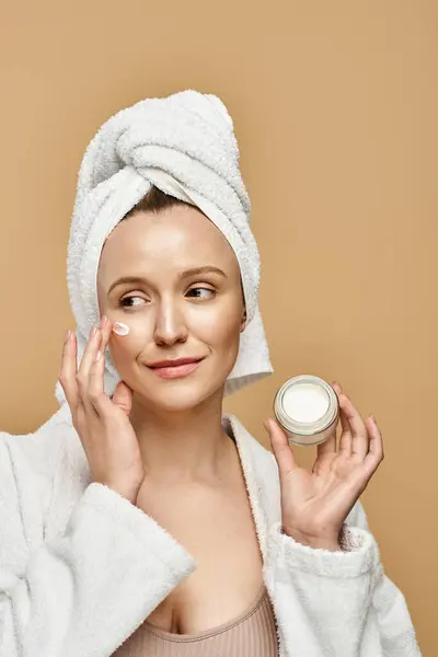 A serene woman with a towel on her head holding a jar of cream. — Stock Photo