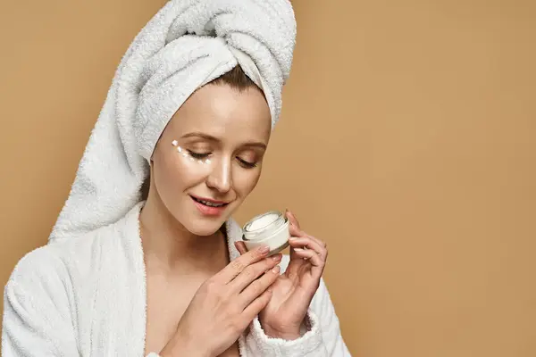 A beautiful woman with a towel on her head holding a jar of cream, showcasing her natural beauty and skincare routine. — Stock Photo