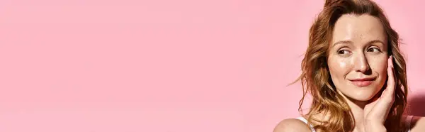 Una donna sorprendente trasuda eleganza mentre posa con grazia di fronte a uno sfondo rosa vibrante. — Foto stock