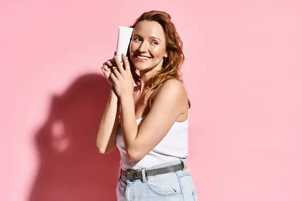 A graceful woman in a white tank top holding cream with focus and ease, embodying natural beauty and modern connectivity. — Stock Photo
