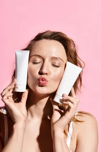 Una hermosa mujer aplica activamente crema de dos tubos en su cara para realzar su belleza natural. - foto de stock
