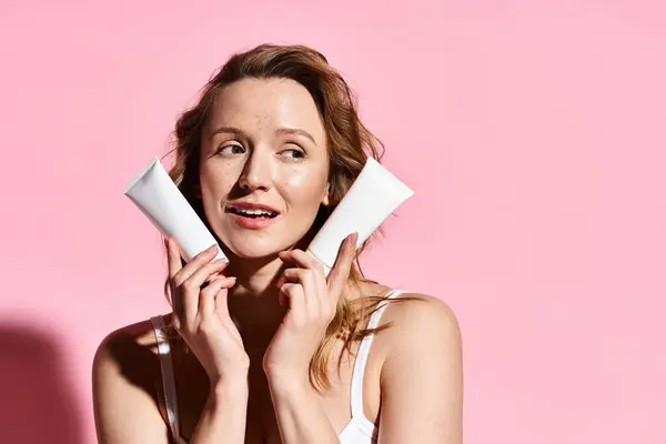 Una donna in canotta bianca che regge con grazia la crema, trasudando bellezza naturale ed eleganza. — Foto stock