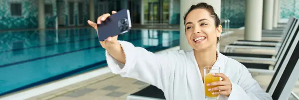 Una joven morena captura un momento sereno junto a la piscina, levantando un teléfono celular para tomar una foto. - foto de stock