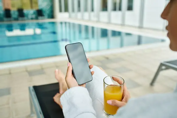 A young, beautiful woman holds a cell phone next to an indoor swimming pool, capturing memories. — Stock Photo