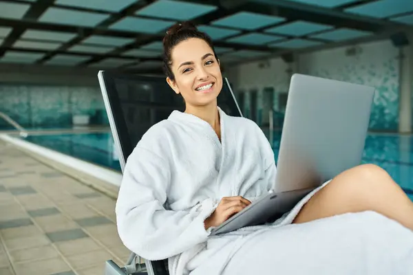 A young, beautiful brunette woman with a laptop, immersed in technology while seated in a comfortable chair. — Stock Photo
