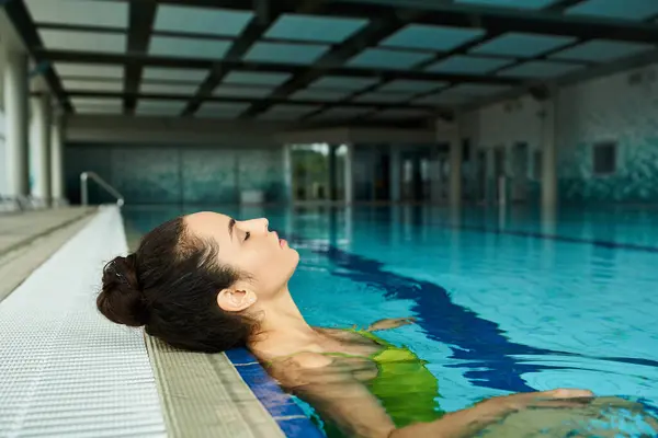 Eine junge, schöne brünette Frau im Badeanzug schwebt mühelos in einem Wellness-Innenpool. — Stockfoto