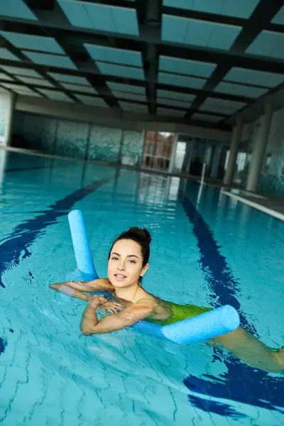Una mujer joven en una piscina, sosteniendo con gracia un salvavidas, exudando calma y seguridad en un entorno de spa interior. - foto de stock