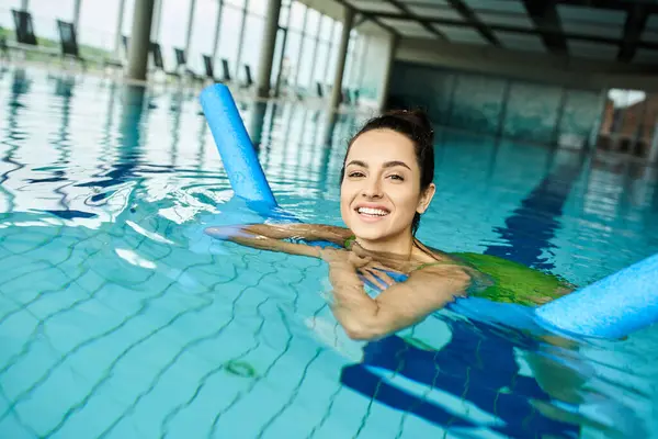 Una joven morena en traje de baño nadando elegantemente en una piscina cubierta - foto de stock
