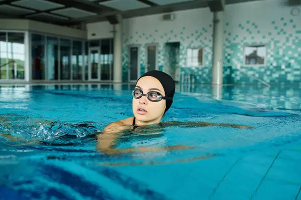 Una mujer en una piscina con gafas, deslizándose tranquilamente por el agua. - foto de stock