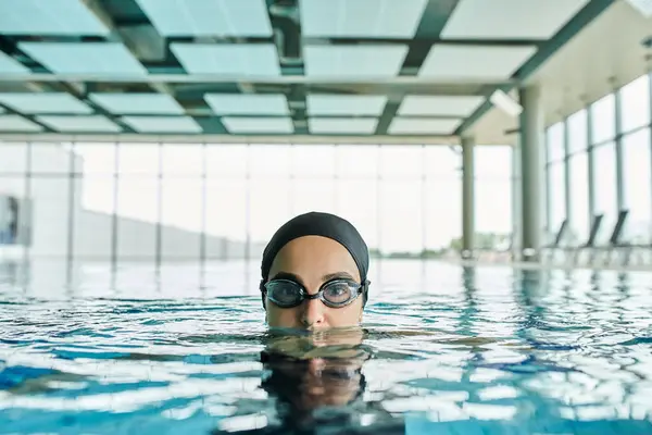Junge Frau gleitet in Schutzbrille und Badekappe durch Pool und verkörpert flüssige Bewegung und Ruhe. — Stockfoto