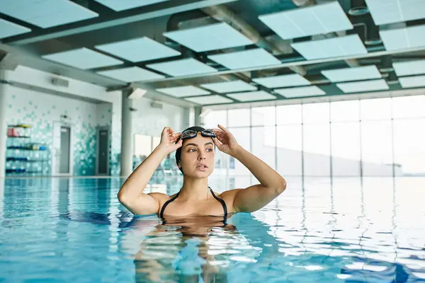Una mujer joven en traje de baño y gorra de natación nadando elegantemente en un spa interior. - foto de stock