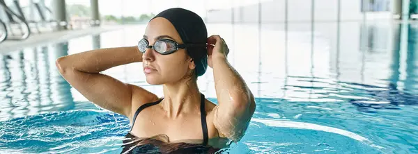 Una mujer joven en traje de baño y gorra de natación nade graciosamente bajo el agua en un spa interior, con gafas. - foto de stock