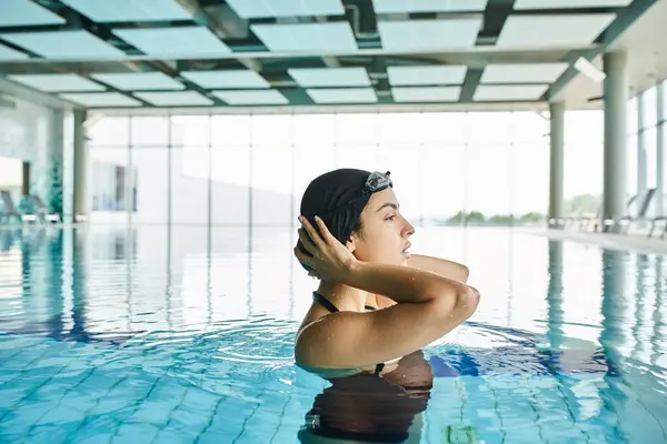 Молодая женщина в купальнике и плавательной шапочке грациозно плавает в крытом спа-салоне в очках. — стоковое фото