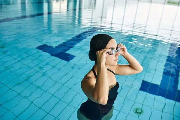 Mujer joven en traje de baño negro y gorra de natación nadando con gracia en una piscina de hidromasaje cubierta. - foto de stock