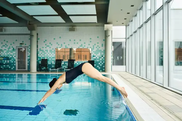 A young woman in a swimsuit and swim cap gracefully dives into a sparkling blue swimming pool. — Stock Photo