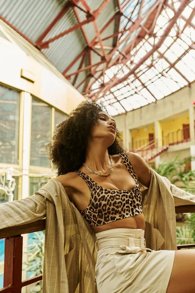 Chic frisé afro-américain femme posant dans sa tenue tendance dans un cadre tropical avec des plantes — Photo de stock