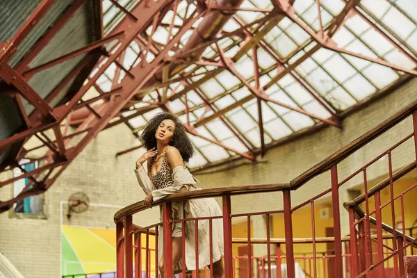 African american woman with curly hair in animal print look posing against industrial backdrop — Stock Photo