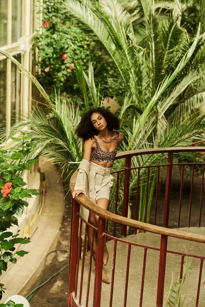 Modische junge schwarze Frau mit lockigem Haar posiert auf einer Brücke im Garten — Stockfoto