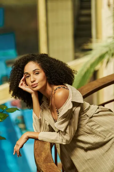 Young african american woman with curly hair leaning on metallic structure in green garden setting — Stock Photo