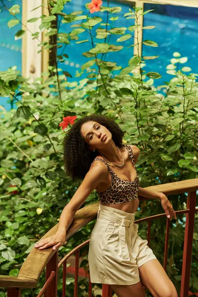 Young african american woman with curly hair posing on metallic bridge in green garden setting — Stock Photo