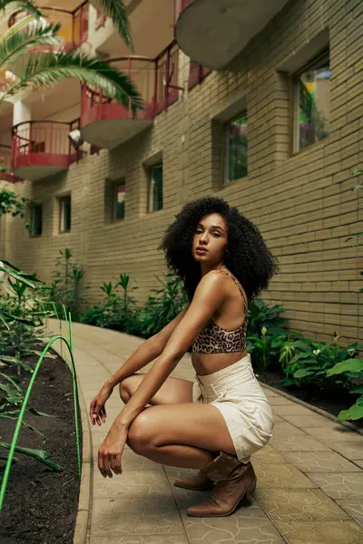 Confident black woman in chic style attire and boots posing in atrium with botanical backdrop — Stock Photo