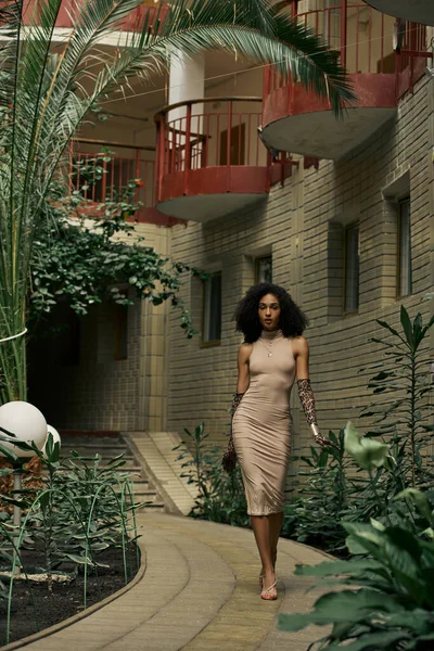 Sofisticata donna afroamericana in abito e guanti stampa animalier passeggiando nel giardino urbano — Foto stock