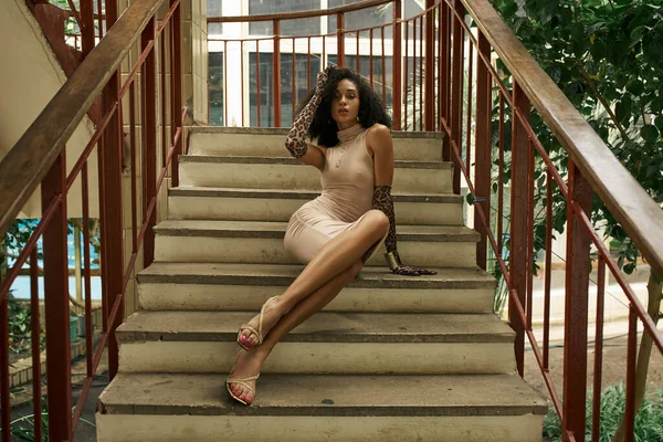 Young black woman in dress and animal print gloves sitting on stairs in urban setting, glamour — Stock Photo