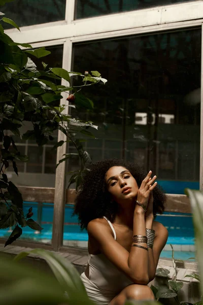 Серединна краса, кучерява афроамериканська жінка позує в білому купальнику в оазисі суворого саду — стокове фото