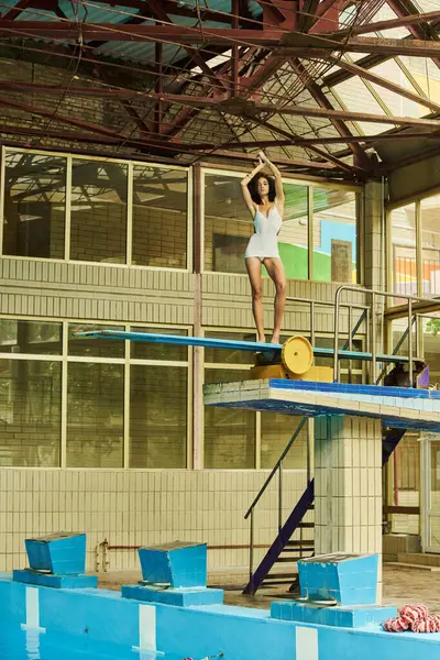 Junge afrikanisch-amerikanische Frau in trendiger Badebekleidung balanciert elegant auf einem Sprungbrett in einem Hallenbad — Stockfoto