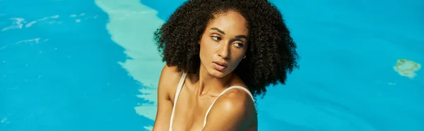 Banner of curly african american woman posing in blue water of swimming pool, looking away — Stock Photo