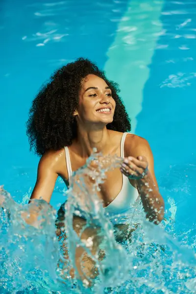 Heureuse femme noire éclaboussant l'eau à l'intérieur de la piscine, se délectant de son plaisir et de plaisir pendant les vacances — Photo de stock