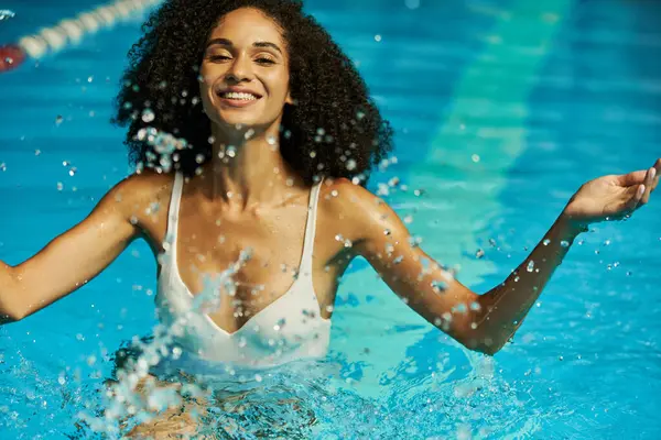 Mulher americana africana alegre espirrando água na piscina, revelando sua alegria e diversão durante as férias — Fotografia de Stock