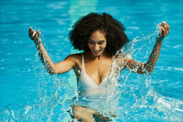 Mulher afro-americana despreocupada salpicando água na piscina, revelando sua alegria e diversão durante as férias — Fotografia de Stock